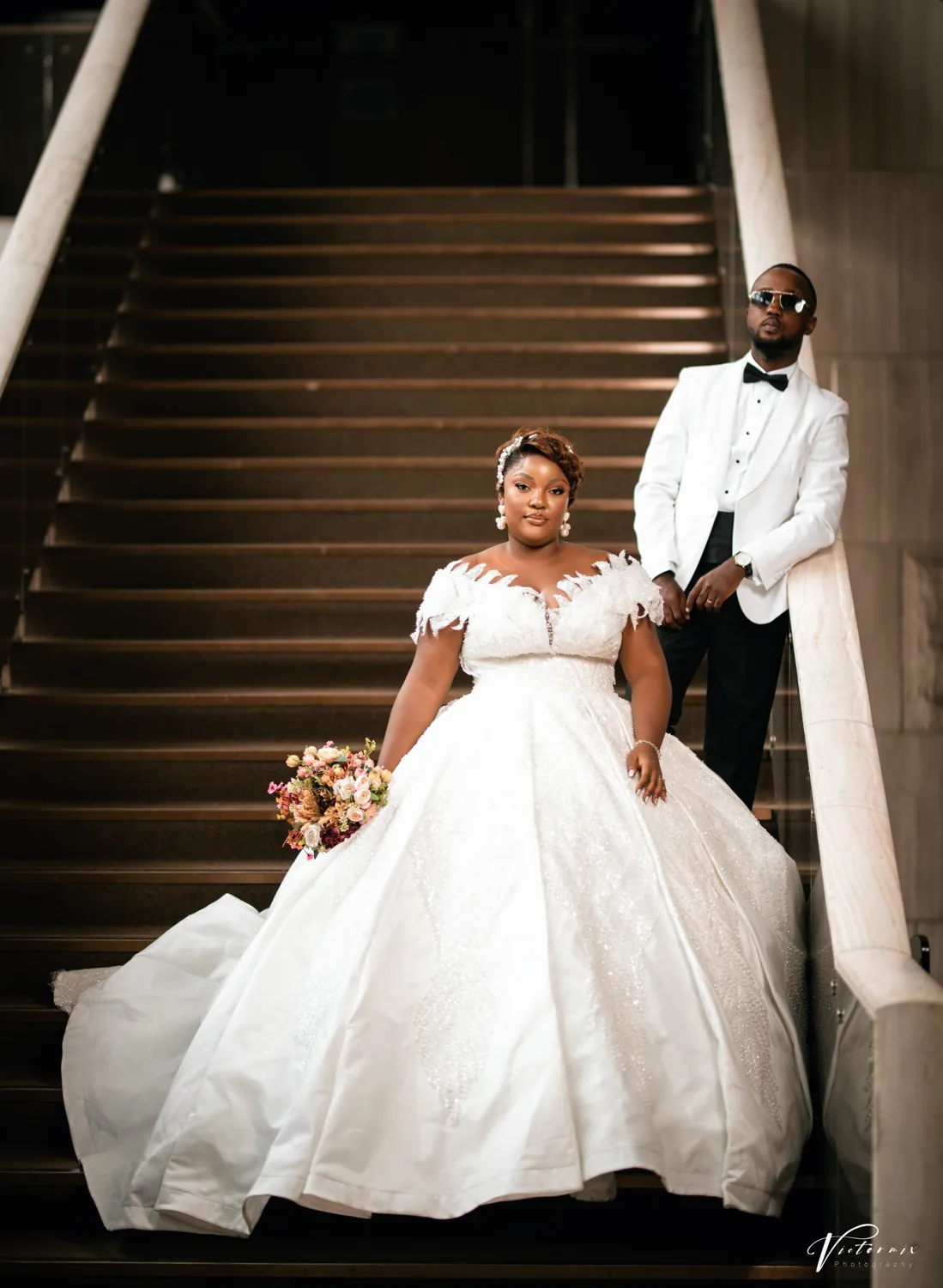 A bride and groom on a dark staircase, her gown spread across the steps.