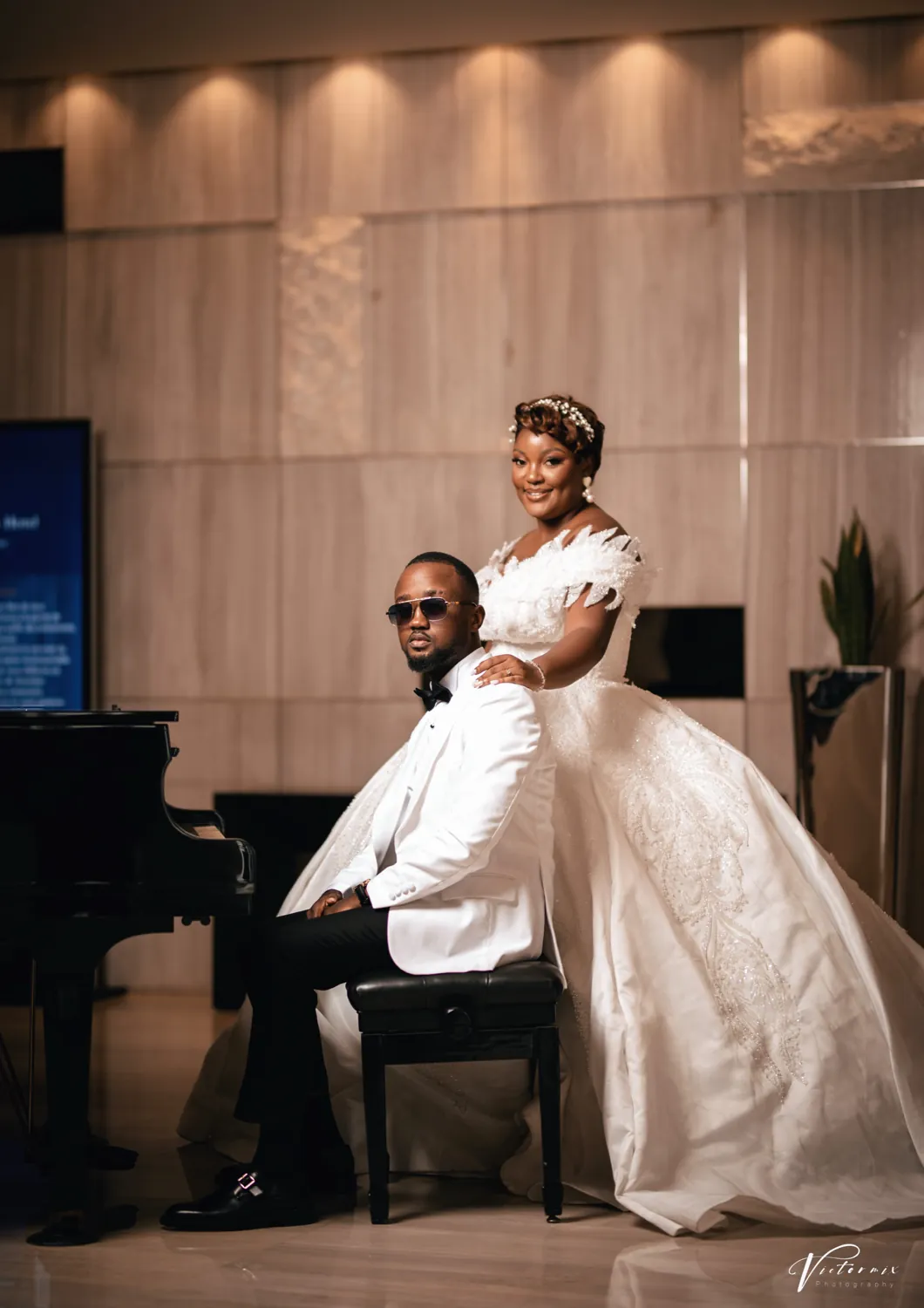 The groom at a piano while the bride leans over him.