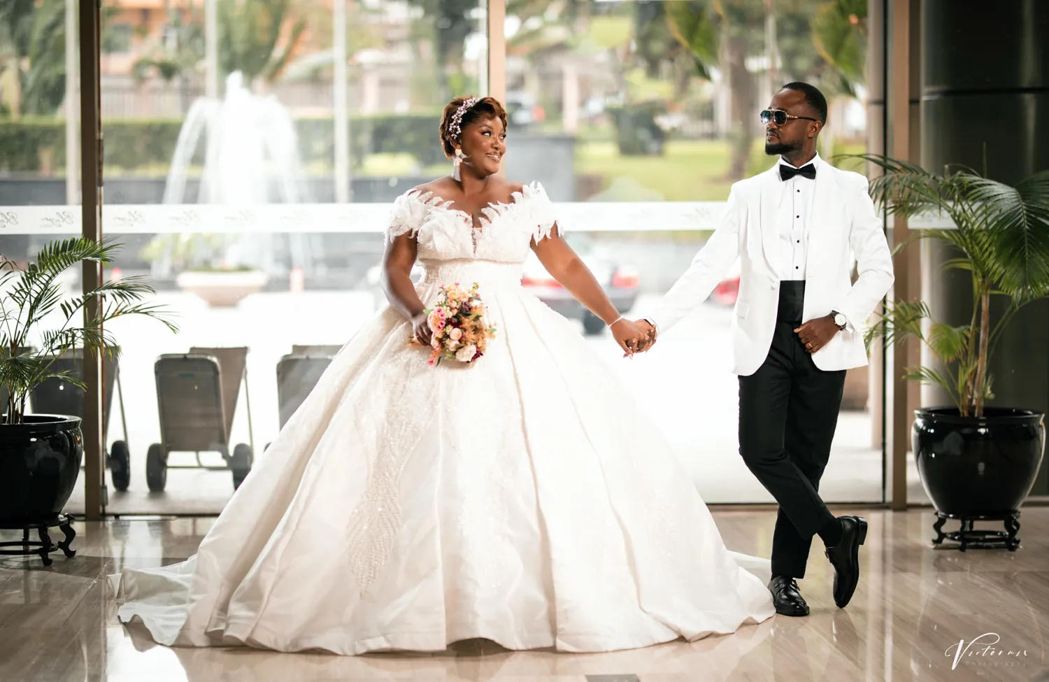 The couple walking hand in hand across a bright hotel lobby.